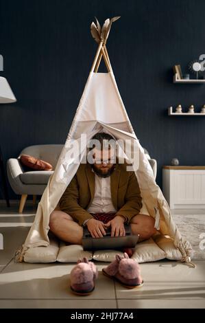 Glücklicher Geschäftsmann, der im Heimzelt mit einem Laptop arbeitet Stockfoto