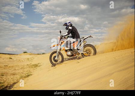 Professioneller Motocross-Fahrer, der den Sandberg hinunterrutscht Stockfoto