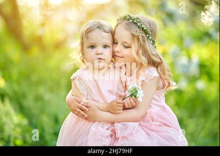 Zwei schöne kleine Mädchen in rosa Kleidern im Park bei Sonnenuntergang. Kinder haben eine Pause im Freien Stockfoto