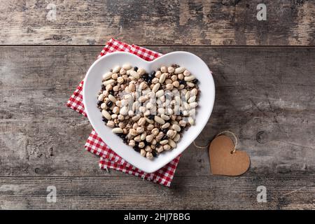 Ungekochte verschiedene Hülsenfrüchte in herzförmiger Platte auf Holztisch Stockfoto