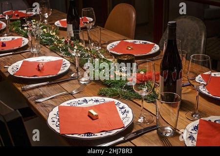 Großer rustikaler Holztisch festlich und dekoriert für ein Abendessen mit Freunden oder Familie, weiß gemusterte Teller, rote Servietten, Wein und Gläser, wählen Stockfoto