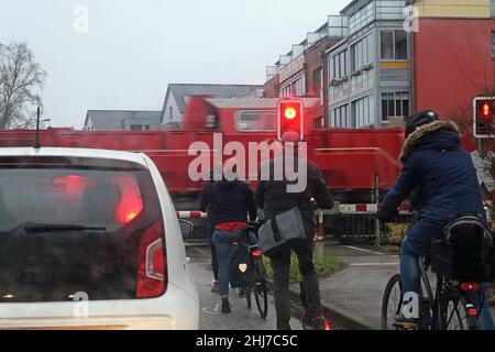 Fahrradfahrer und ein Auto warten vor der geschlossenen Schranke und der roten Ampel, weil ein Zug vorbeifährt, an einem kalten Morgen zur Hauptverkehrszeit Stockfoto