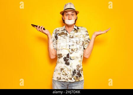 Männlicher Touristenreisender mit Klebeband über dem Mund kann nicht telefonieren, versteht Probleme nicht Stockfoto