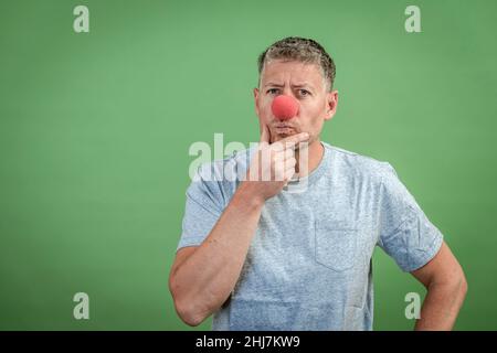 Mann mit roter Clownsnase und grauem Hemd vor grünem Hintergrund Stockfoto