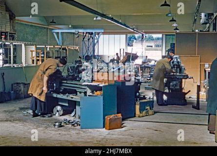 Männer arbeiten in einer kürzlich erbauten Industrieanlage im Industriegebiet Crawley ‘New Town’, West Sussex, England, UK c. 1960. Die Metallbearbeitungswerkzeuge, die sie verwenden, umfassen eine Drehmaschine und einen Bohrer. Eine große Tür, die nach hinten offen ist, blickt auf ein anderes Industriegebäude, das gerade gebaut wird. Crawleys Industriegebiet konzentrierte sich hauptsächlich auf den Norden des Stadtzentrums. Es wurde entwickelt, um Arbeitsplätze in der ‘neuen Stadt’ der Nachkriegszeit zu schaffen. Seit dieser Zeit hat sich das Gebiet massiv verändert und modernisiert. Dieses Bild stammt aus einer alten Amateur-Farbtransparenz – einem Vintage-Foto aus dem Jahr 1950s/1960s. Stockfoto