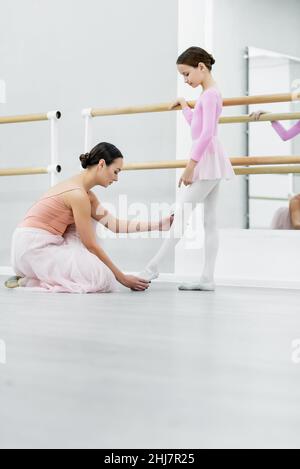 Seitenansicht der Tanzlehrerin, die das Bein des Mädchentrainings in der Ballettschule berührt Stockfoto