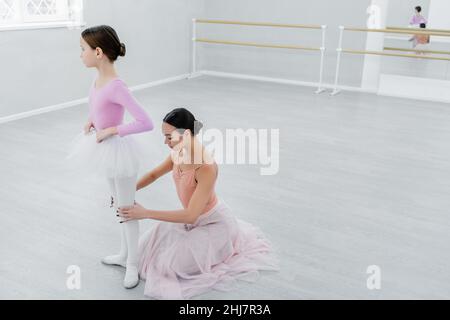 Ballettmeister berührt die Knie des Mädchens während der Probe im Tanzsaal Stockfoto