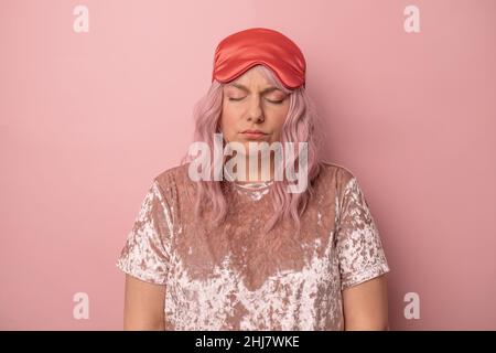 Verärgert schläfrige Frau mit geschlossenen Augen trägt Schlafmaske, traurig, früh morgens isoliert über rosa Hintergrund aufzuwachen. Stockfoto