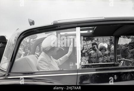 1977, historische, glückliche Gesichter und Gewerkschaftsflaggen, während wir Nahaufnahme sehen, sitzen Ihre Majestät, Königin Elizabeth II. Und Prinz Phlip in ihrem offiziellen Staatsfahrzeug, einem Rolls-Royce Phanton VI, und winken den Massen am Straßenrand, London, England, Großbritannien, während der Silver Jubliee-Feierlichkeiten zu. Stockfoto