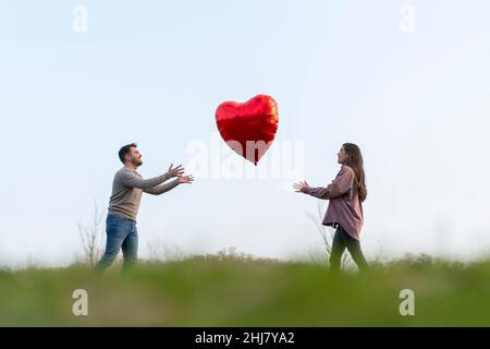 Das junge Paar feiert den valentinstag und spielt mit einem herzförmigen Ballon Stockfoto