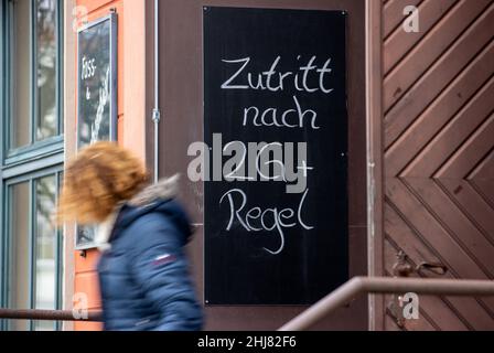 Greifswald, Deutschland. 27th Januar 2022. Eine Frau verlässt ein Restaurant mit einem Schild über die Corona-Regeln, das neben der Tür hängt. (To dpa 'Neue Corona-Landesverordnung bringt zahlreiche Änderungen') Quelle: Jens Büttner/dpa-Zentralbild/dpa/Alamy Live News Stockfoto