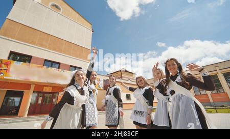 Glückliche russische Schulabgänger strecken sich an ihrem letzten Schultag die Hände. Stockfoto