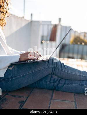Nahaufnahme einer unkenntlichen Frau, die mit ihrem Laptop auf dem Boden auf der Terrasse sitzt Stockfoto