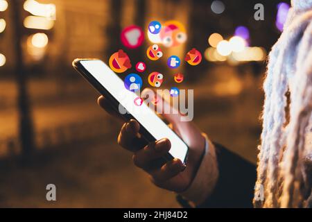 Social Media User Interaction Konzept, weibliche Hand halten Smartphone mit Emoji, Likes, Follower und Kontakte Symbole Stockfoto