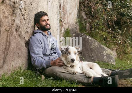 Hispanischer Mann und brauner Border Collie lieben sich im Freien Stockfoto