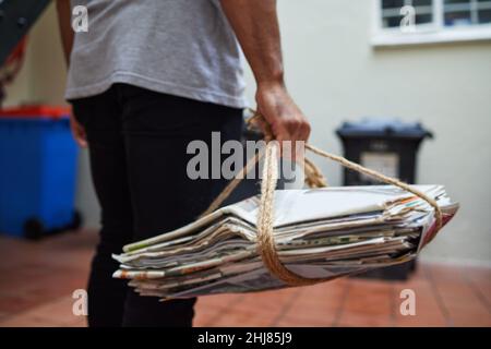 Recyceln, um unseren Planeten zu schützen. Eine ausgeschnittene Aufnahme eines unkenntlichen Mannes, der zu Hause Zeitung recycelt. Stockfoto