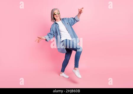 Ganzkörper-Foto von verrückten gealterten Dame Tanz tragen blauen Blazer Jeans Sneakers isoliert auf rosa Hintergrund Stockfoto