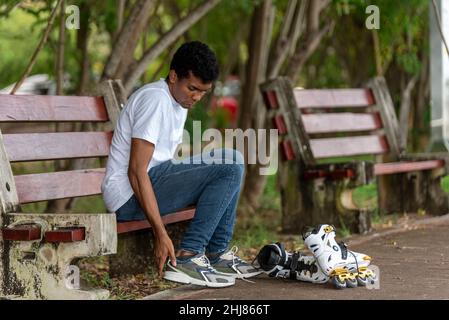 Junger Latino-Mann, der auf Inline-Skates sitzt Stockfoto
