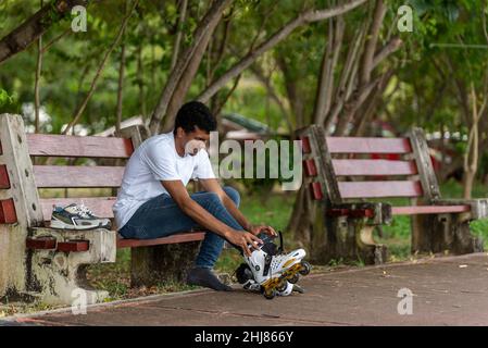 Junger Latino-Mann, der auf Inline-Skates sitzt Stockfoto