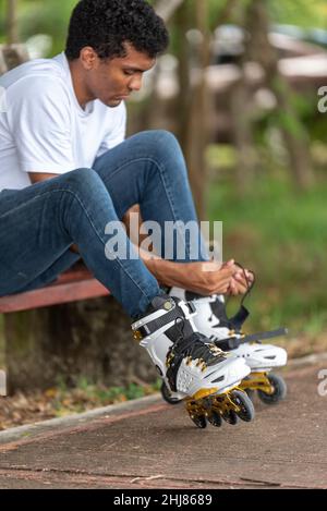 Junger Latino-Mann, der auf Inline-Skates sitzt Stockfoto