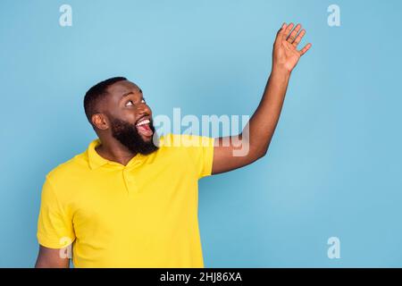 Foto von beeindruckt süßen dunklen Haut Kerl gekleidet gelben T-Shirt Arme suchen leeren Raum isoliert blauen Hintergrund Stockfoto