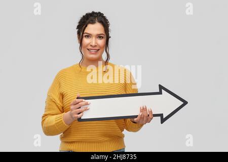 Lächelnde junge Frau mit großem weißen Pfeil nach rechts Stockfoto