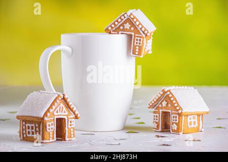 Lebkuchenhütten und eine Tasse Milch auf einer weißen Betonoberfläche mit Funkeln, Nahaufnahme. Weihnachtsfeier Konzept Stockfoto