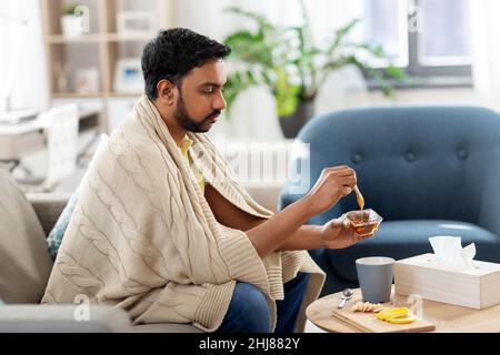 Kranker junger Mann in einer Decke, der zu Hause heißen Tee trinkt Stockfoto