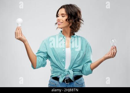 Lächelnde Frau, die verschiedene Glühbirnen vergleicht Stockfoto
