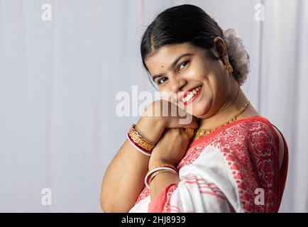 Eine indische Frau in rotem Saree trägt Armreifen mit lächelndem Gesicht auf weißem Hintergrund Stockfoto