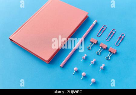 Pinkes Notizbuch, Stifte, Clips und Bleistift auf Blau Stockfoto