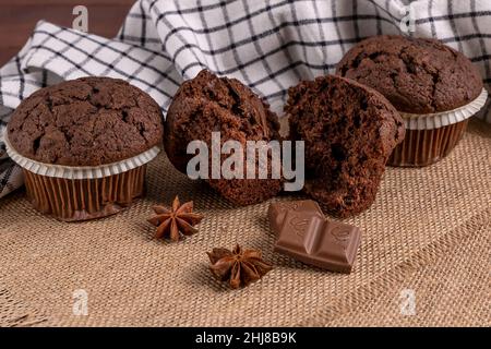 Köstliche Schokoladen-Muffins mit quadratischer Schokolade und Sternanismuffins auf Jute-Matte Stockfoto