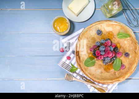 Russische ukrainische europäischen Feiertag Maslenitsa. Traditionelle dünne Crepes-Pfannkuchen, mit Belag aus Berrry, Marmelade und Honig auf blauem Holztisch, Blick von oben CO Stockfoto