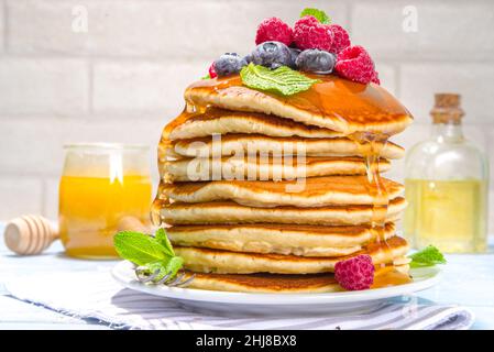 Teller mit leckeren traditionellen amerikanischen Pfannkuchen mit frischen Beeren und Sirup auf Küchentisch auf hellem Hintergrund Stockfoto