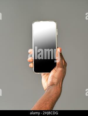 afroamerikanischer Mann hält Smartphone mit schwarzem Bildschirm an der Kamera. Gesperrter Bildschirm Smartphone in afrikanischen Mann Hand isoliert auf grauem Hintergrund. Stockfoto