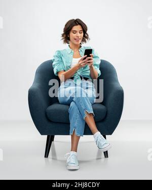 Glückliche Frau mit Smartphone im Sessel sitzend Stockfoto