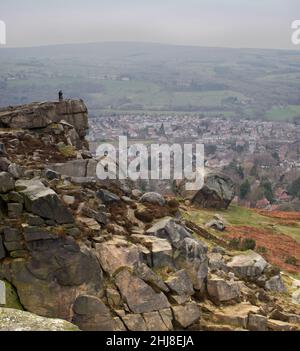 Menschen, die am Rand der Cow and Calf-Felsformation stehen und auf die Stadt Ilkley zeigen, darunter Stockfoto