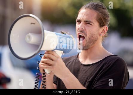 Auf mein Ziel hinarbeiten. Aufnahme eines jungen Mannes mit einem Megaphon bei einer Protestkundgebung. Stockfoto