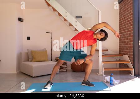 Die ganze Länge des afroamerikanischen jungen Mannes macht Stretching-Übungen auf der Matte zu Hause. Unverändert, Fitness, Getränk und aktiven Lebensstil Konzept. Stockfoto
