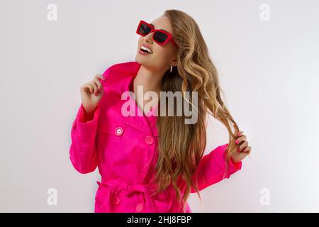 Close up glückliches Mädchen in roten Sonnenbrillen und rosa Mantel isoliert auf weißem Hintergrund. Aufgeregt, Schock und überrascht junge Frau in trendigen Outfit. Mode A