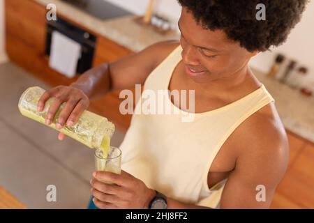 Hochwinkelansicht eines lächelnden afroamerikanischen jungen Mannes, der Smoothie in Trinkglas gießt. Unverfälscht, Influencer, gesundes Essen, organisches und gesundes lif Stockfoto