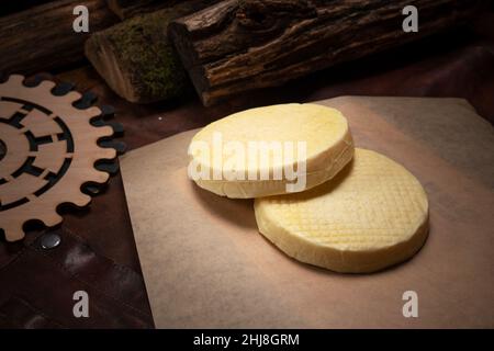 Mehrere Ziegenkäseräder übereinander auf kunstvoll gearbeiteter Papier- und Holzdekoration. Ziegenkäse mit niedrigem Laktosegehalt. Weicher Ziegenkäse aus gepresstem Käseschott. Stockfoto