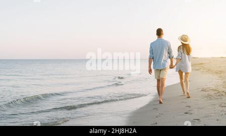 Romantisches junges verliebte Paar, das bei Sonnenuntergang an einem mediterranen Strand entlang spazierengeht. Sommerurlaub in einem warmen Land. Glückliches Ehepaar Stockfoto