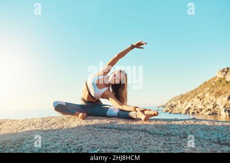 Mach dich nicht nur fit, sondern gesund. Aufnahme einer athletischen jungen Frau, die am Strand Yoga praktiziert. Stockfoto