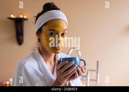 Portrait der lächelnden biracial junge Frau mit gelben Gesichtsmaske Kaffee im Spa. Unverändert, Spa, Körperpflege, Lebensstil, Vitiligo und Wellness. Stockfoto
