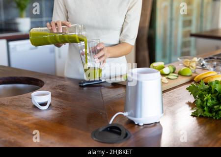 Mittelteil der biracial junge Frau Gießen Fruchtsaft aus Mixbecher in Trinkglas zu Hause. Unverändert, Lebensstil, Vitiligo und gesunde Ernährung con Stockfoto