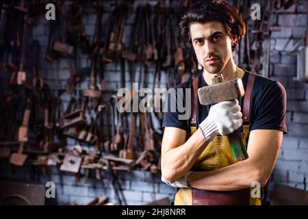 Authentischer Schmied schmiedet ein Metallprodukt in dunklen Innenräumen Studio Stockfoto