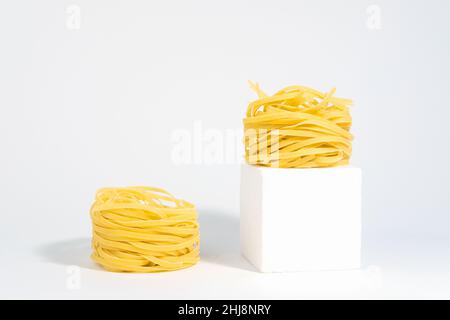 Italienische Pasta. Spaghetti Capellini, auf einem weißen Podium, isoliert auf einem weißgrauen Hintergrund, mit harten Schatten. Pasta in Form von Nestern. Kreativer ph-Wert Stockfoto