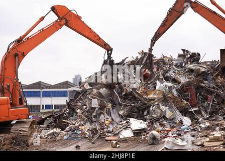 Industrielle Neuverwendung. Ausgeschnittene Aufnahme von zwei Baggern, die durch einen Haufen von Metallschrott sortieren. Stockfoto