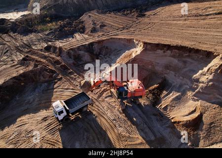 Der Bagger lädt den Sand in einen Muldenkipper im Tagebau. Entwicklung des Sandes im Tagebaus. Schwere Maschinen auf Erdarbeiten im Steinbruch. Miningtruck Stockfoto